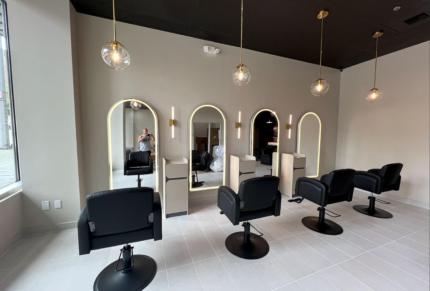 Styling stations with arched backlit mirrors and brass pendant lights at Liana Hair Salon, Seattle